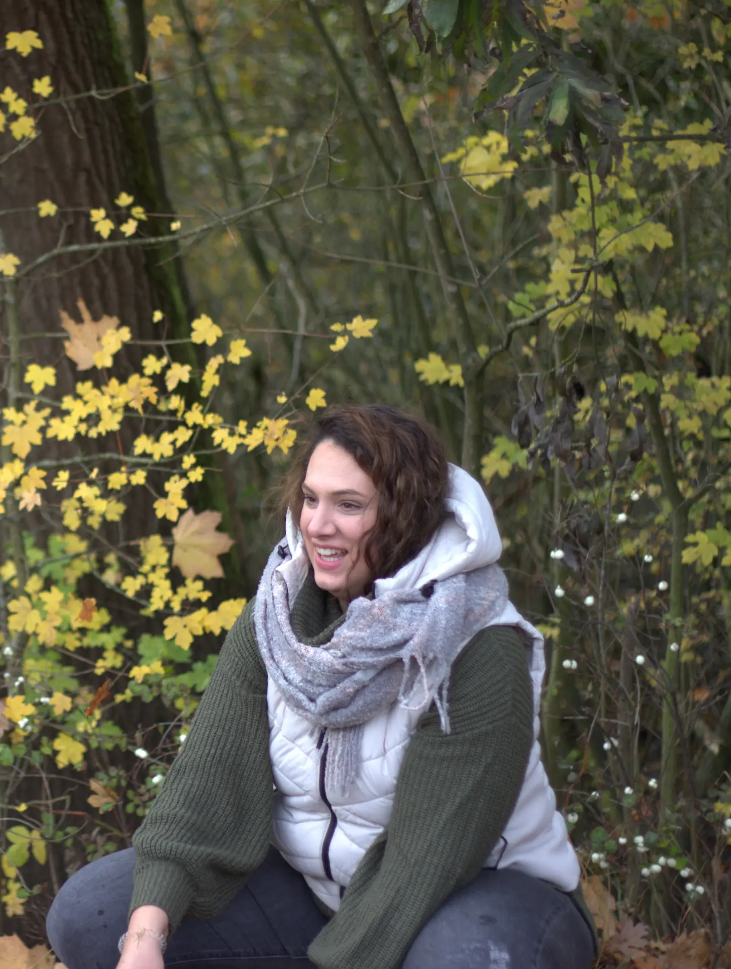 Familienberaterin sitzt am Baum auf dem Boden und blickt ruhig in die Ferne – ein Moment der Reflexion und inneren Klarheit.